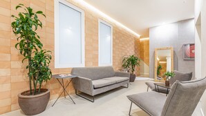 Ein moderner Wartebereich mit einem grauen Sofa, einem Sessel, einem kleinen Tisch und zwei Zimmerpflanzen.
