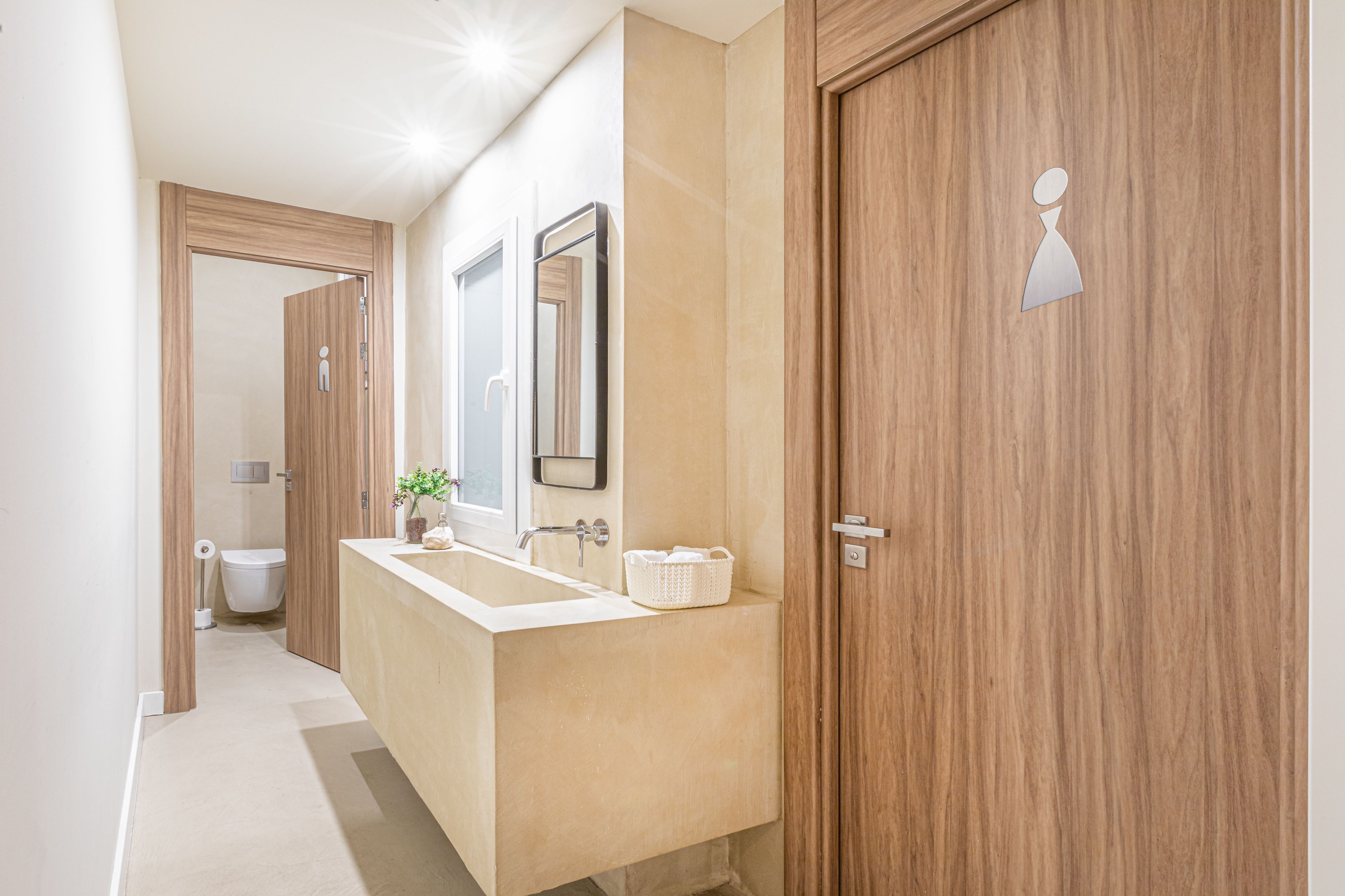 Une salle de bain moderne avec un meuble-lavabo en bois, un grand miroir et des toilettes visibles au fond.