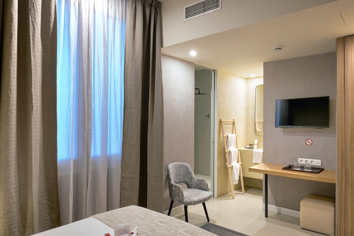 Ein Hotelzimmer mit Bett, Schreibtisch mit Fernseher, Stuhl und einem durchgehenden Türspalte sichtbaren Badezimmer.