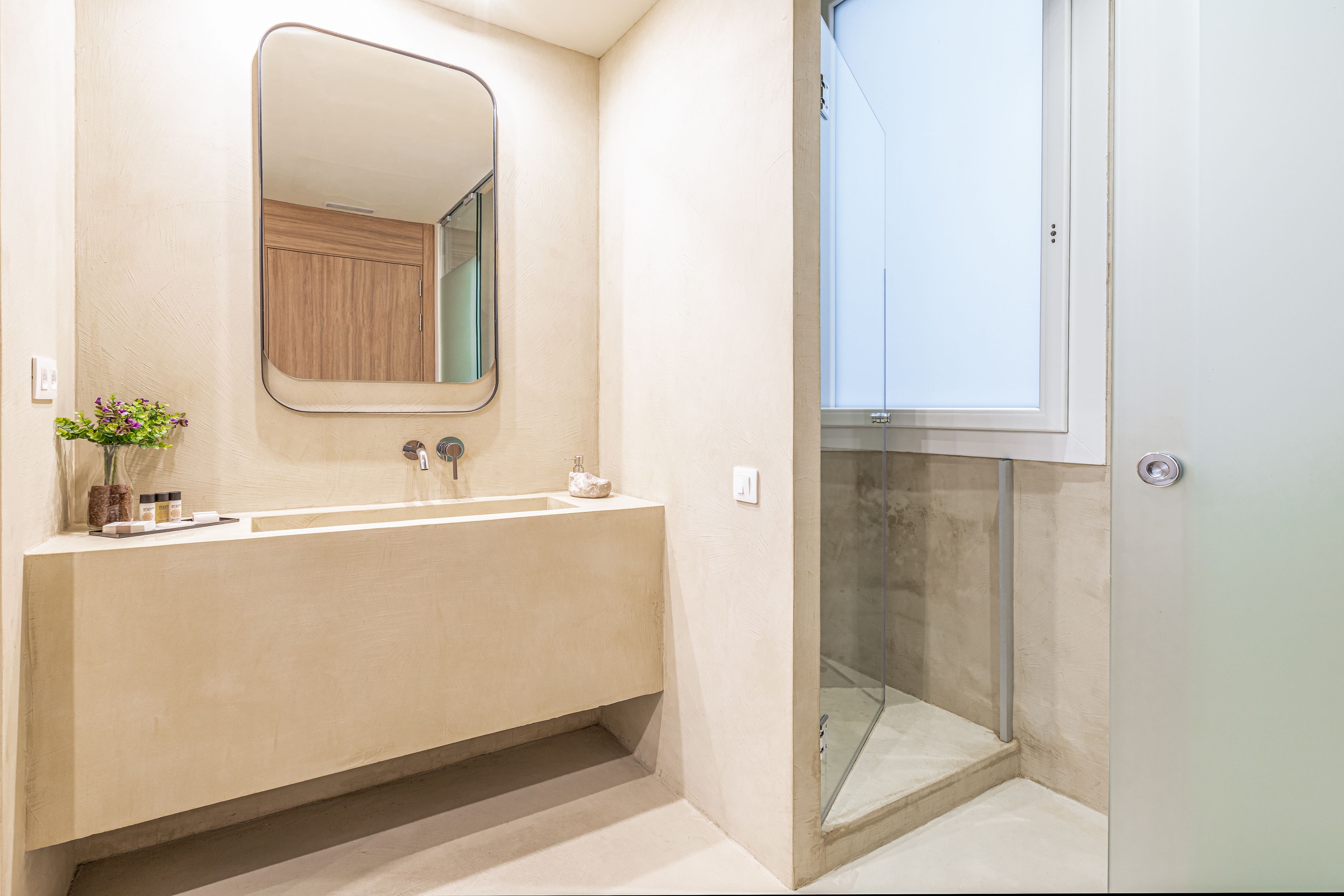 Une salle de bain avec un grand lavabo, un miroir, une cabine de douche en verre et une porte.
