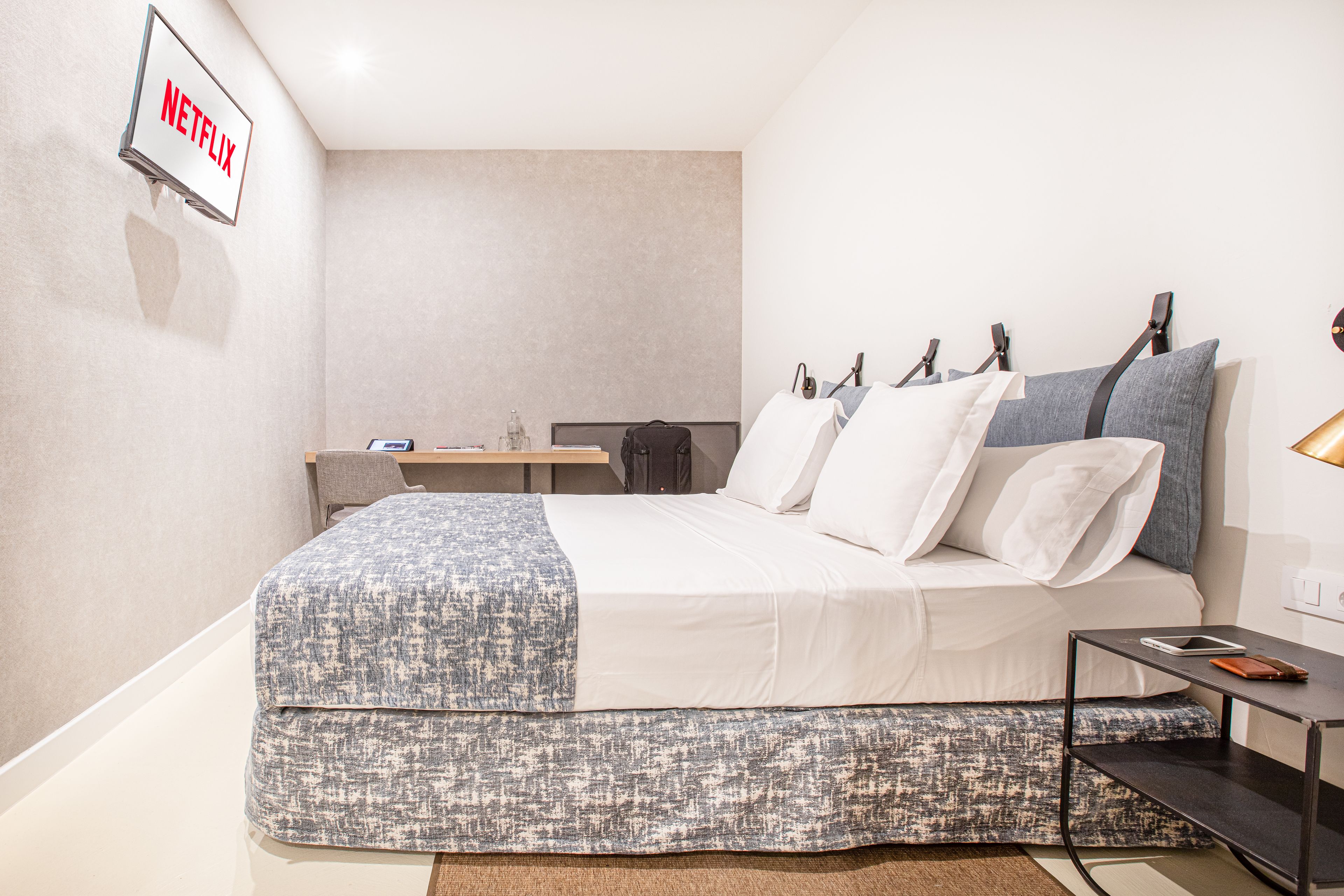 Una habitación de hotel moderna con una cama bien hecha, un escritorio pequeño y un televisor de pared que muestra el logotipo de Netflix.