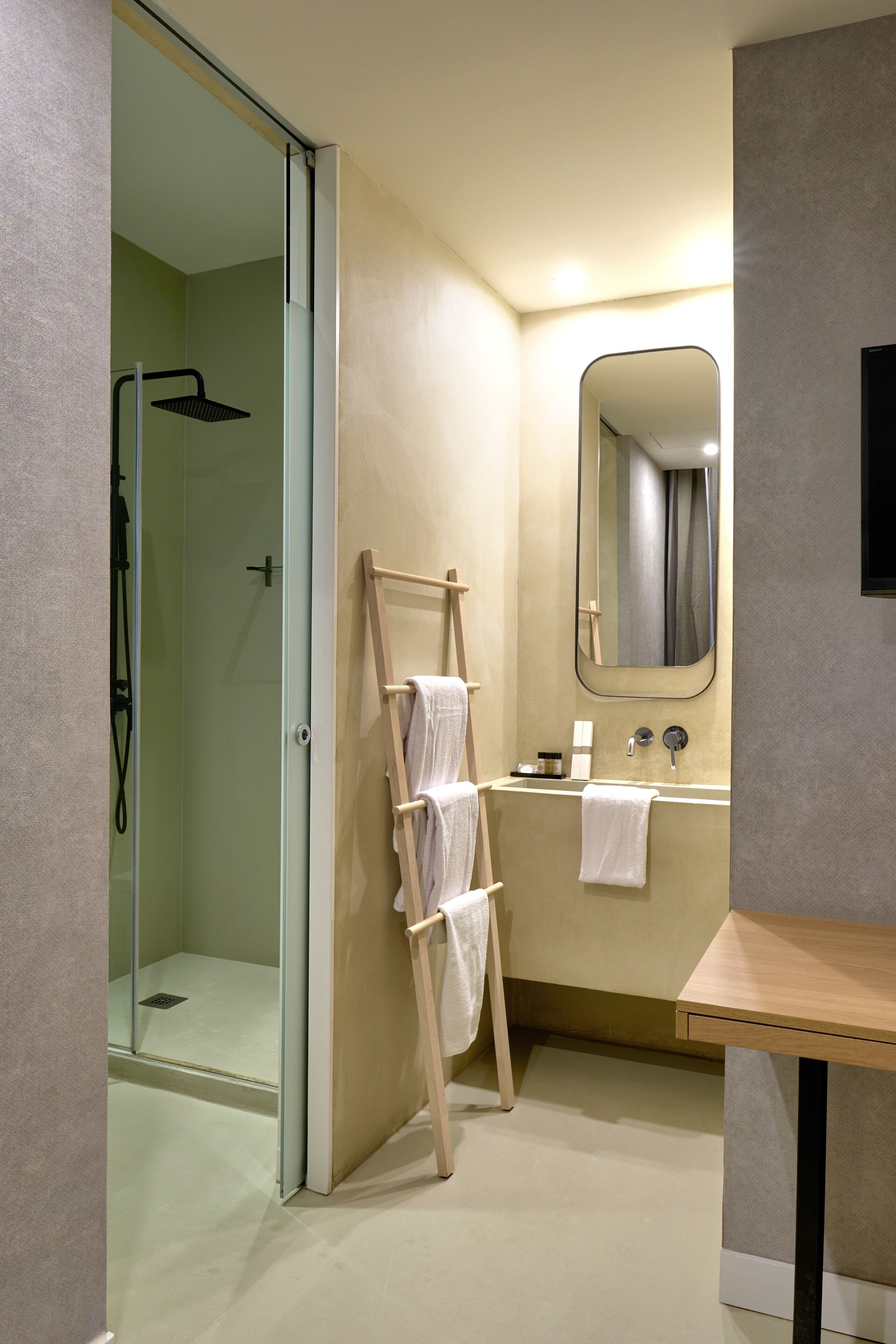 Un baño moderno con ducha envuelta en vidrio, un perchero de madera, un lavabo con espejo y un mueble de tocador de madera.