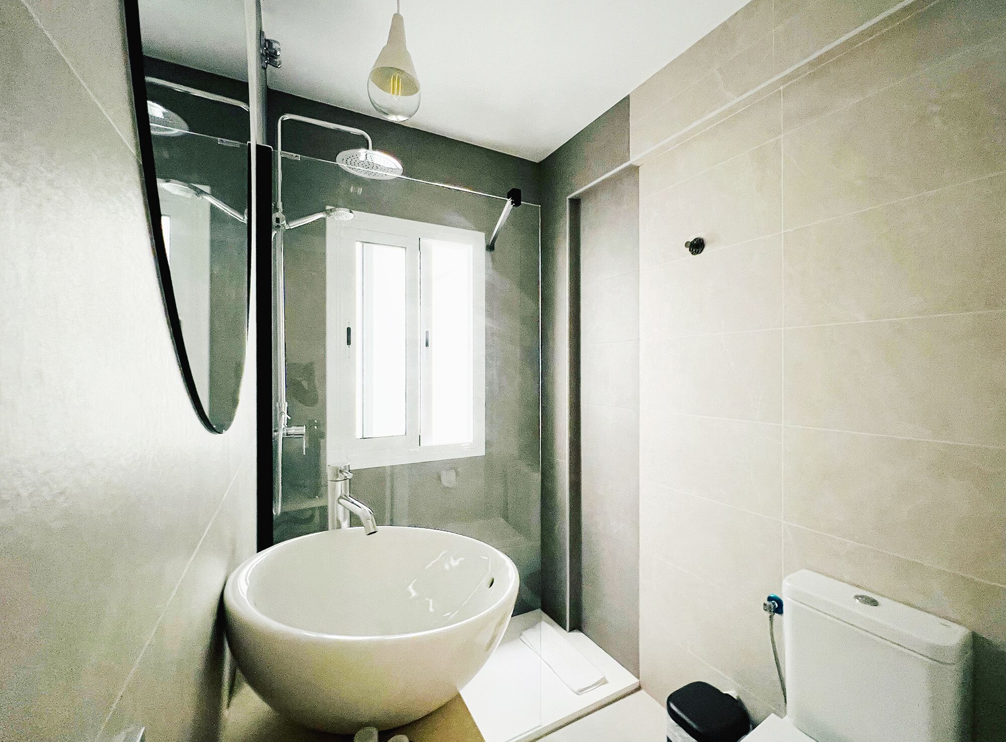 A modern bathroom with a large white sink, a glass shower enclosure, and a toilet.
