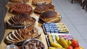 A long wooden table with various food items and condiments, including bread, fruits, and jars of preserved foods. - Pousada Abraco Serrano (Urubici)