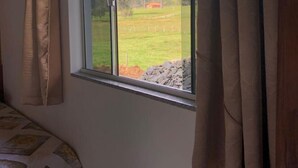 A bedroom with a large window, curtains, and a bed with patterned bedding. - Pousada Abraco Serrano (Urubici)