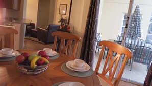 A dining area with a wooden table set for two, a fruit bowl, and a view of the outside balcony. - Kissimmee Area Deluxe Homes by Sunny OVH (Kissimmee)