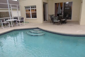 Ein Pool mit Stufen, eine Terrasse mit Stühlen und Tisch sowie eine Glastür.