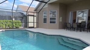 A swimming pool with clear blue water, surrounded by a covered patio area with chairs and a table. - Kissimmee Area Deluxe Homes by Sunny OVH (Kissimmee)