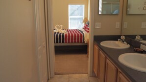 A bedroom with a bed, a window, and a bathroom with two sinks and a mirror. - Kissimmee Area Deluxe Homes by Sunny OVH (Kissimmee)