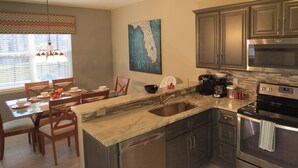 A kitchen with a granite countertop, stainless steel appliances, and a dining area with a table and chairs. - Kissimmee Area Deluxe Homes by Sunny OVH (Kissimmee)