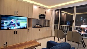 Un salon moderne doté d’un téléviseur à écran plat, d’une table basse en bois, de canapés bleus et d’un balcon offrant une vue sur la ville.