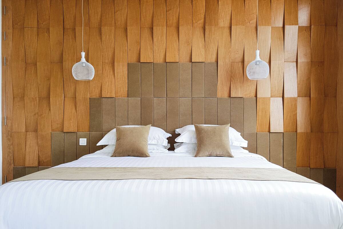 A neatly made bed with white linens and two beige pillows, set against a wooden headboard with a geometric pattern.