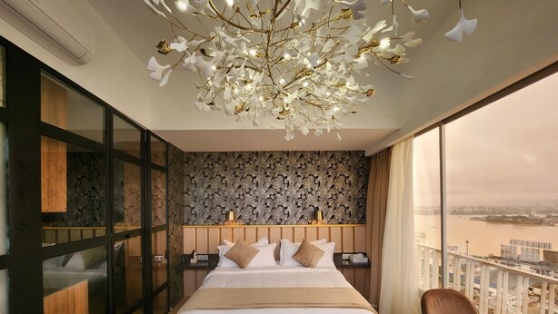 Une chambre d’hôtel moderne avec un grand lit, une vue sur une rivière et un balcon équipé d’une table et d’une chaise.