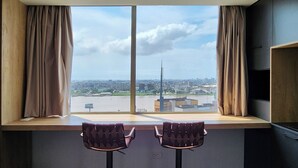 Une pièce dotée d’une grande fenêtre donnant sur un paysage urbain, avec deux tabourets de bar et une vue sur une haute tour.