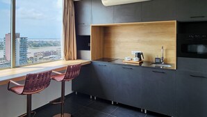 Une cuisine moderne avec un plan de travail en bois, deux tabourets de bar et une vue sur la ville grâce à une grande fenêtre.
