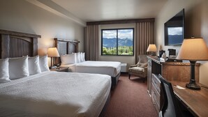 Habitación de hotel con dos camas, un escritorio, una silla, un televisor y una ventana con vista a la montaña.