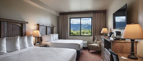 Habitación de hotel con dos camas, un escritorio, una silla, un televisor y una ventana con vista a la montaña.