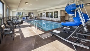 Una piscina con un tobogán azul, sillas de descanso y un área de estar con mesas y sillas.