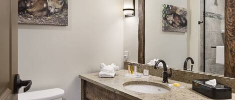 A bathroom with a toilet, sink, and mirror. There are towels and toiletries on the counter.