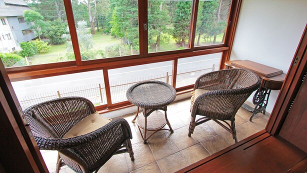 A balcony with wicker furniture, a small table, and a view of a residential area with trees and a fence. - My Home - Titisee (Gramado)
