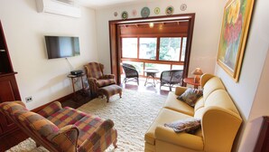 A living room with a sofa, two armchairs, a TV, and a window with a view. - My Home - Titisee (Gramado)