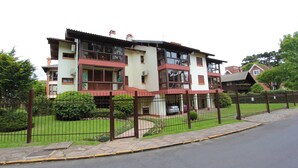 A multi-story residential building with a fenced yard, a paved driveway, and a visible car parked in front. - My Home - Titisee (Gramado)
