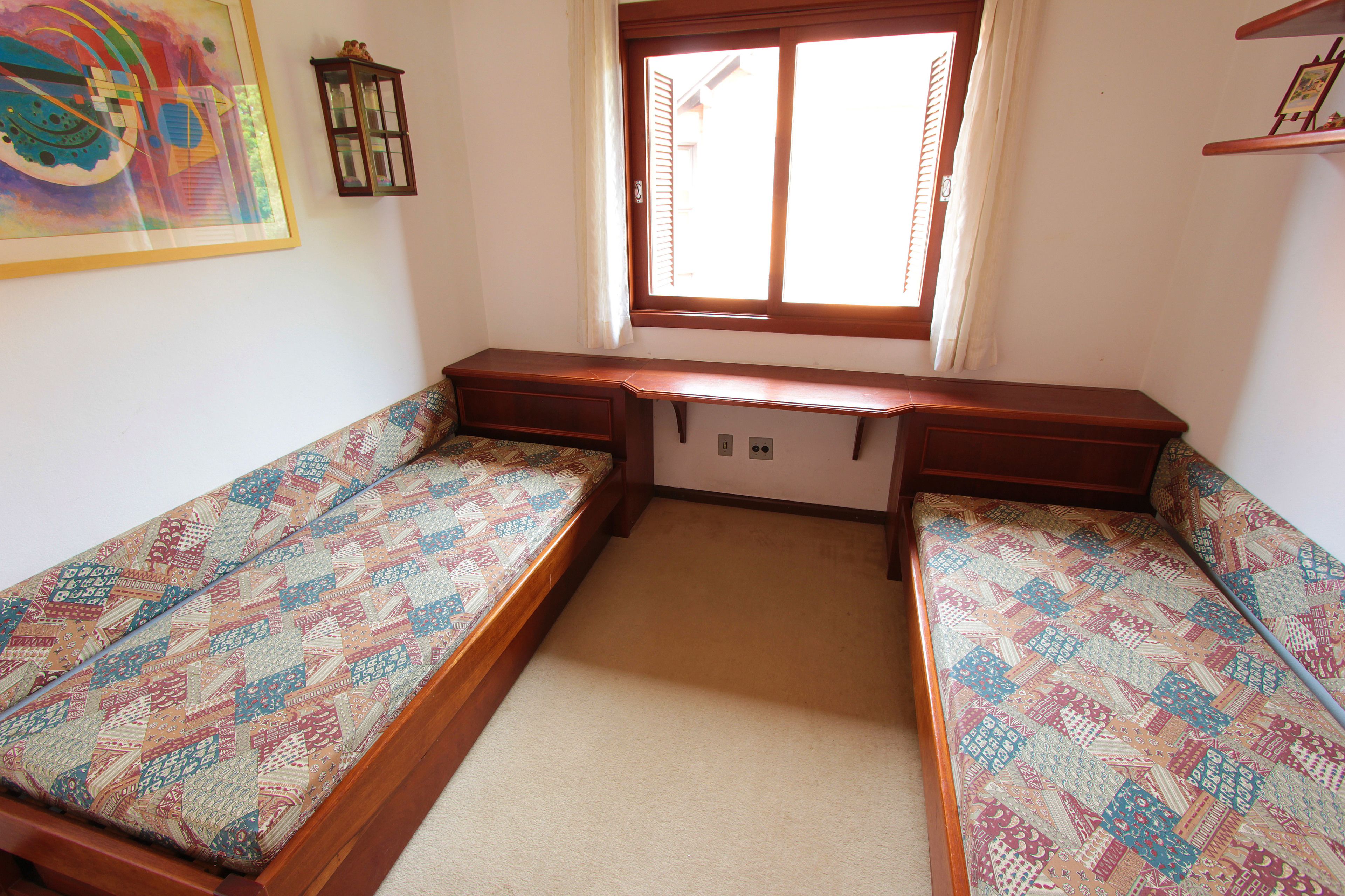 A room with two single beds, a window with blinds, a wall-mounted shelf, and a framed picture.