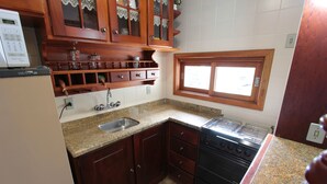 A kitchen with wooden cabinets, a granite countertop, a sink, a stove, and a window. - My Home - Titisee (Gramado)