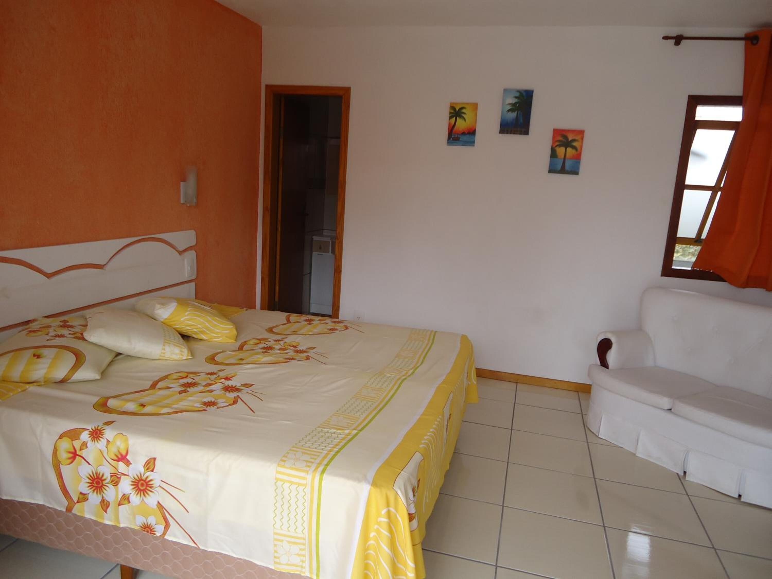 A bedroom with a bed, a white sofa, and three paintings on the wall.
