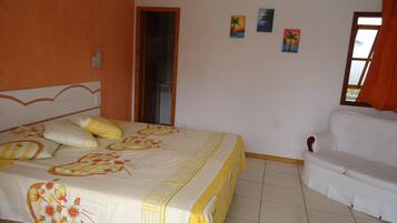 A bedroom with a bed, a white sofa, and three paintings on the wall.