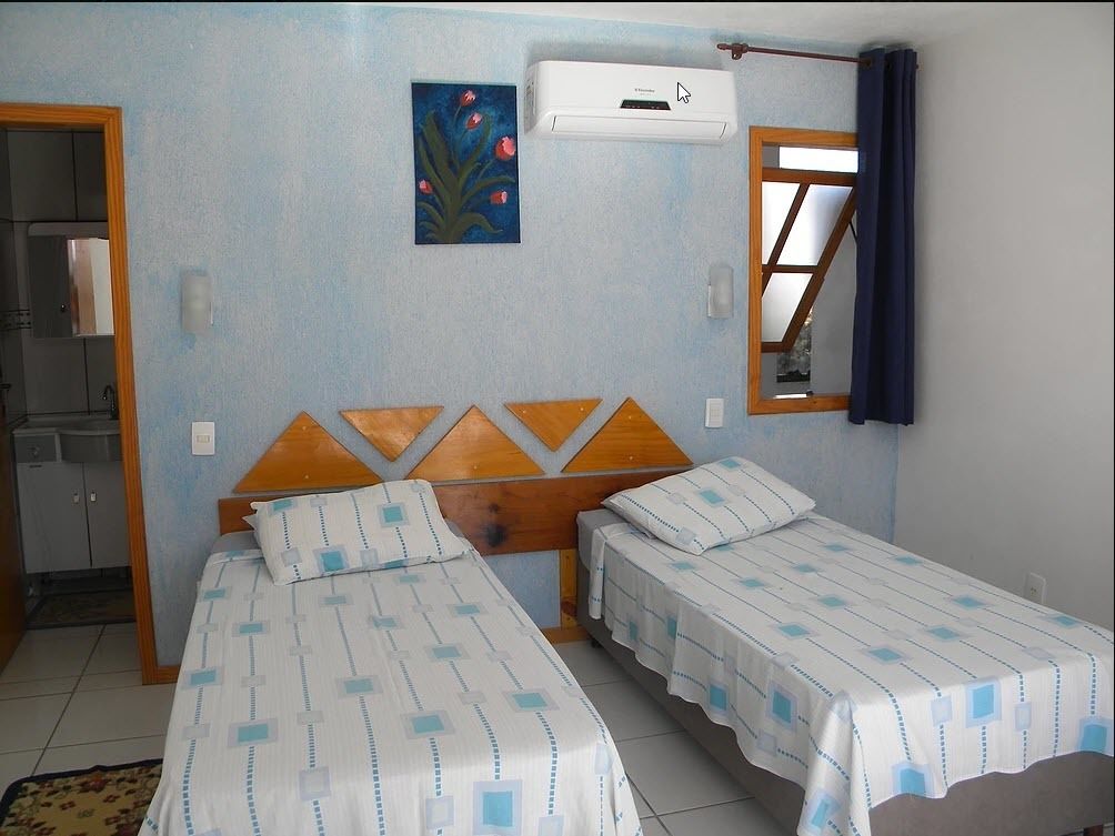 Una habitación con dos camas individuales, un cabecero de madera, un cuadro, un equipo de aire acondicionado y una ventana con cortinas.