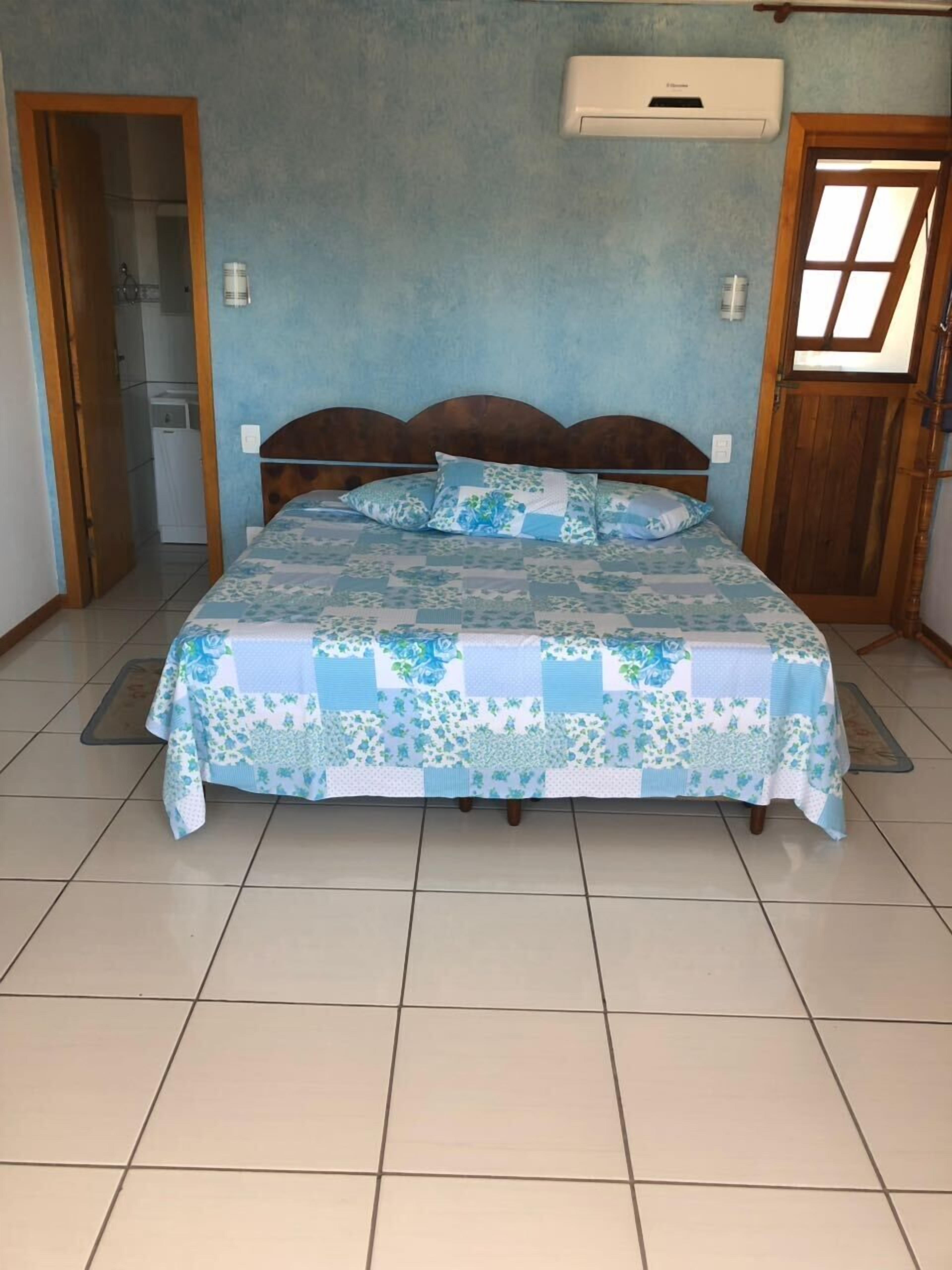 A bedroom with a bed, a wooden headboard, a blue wall, and a window with a wooden frame.