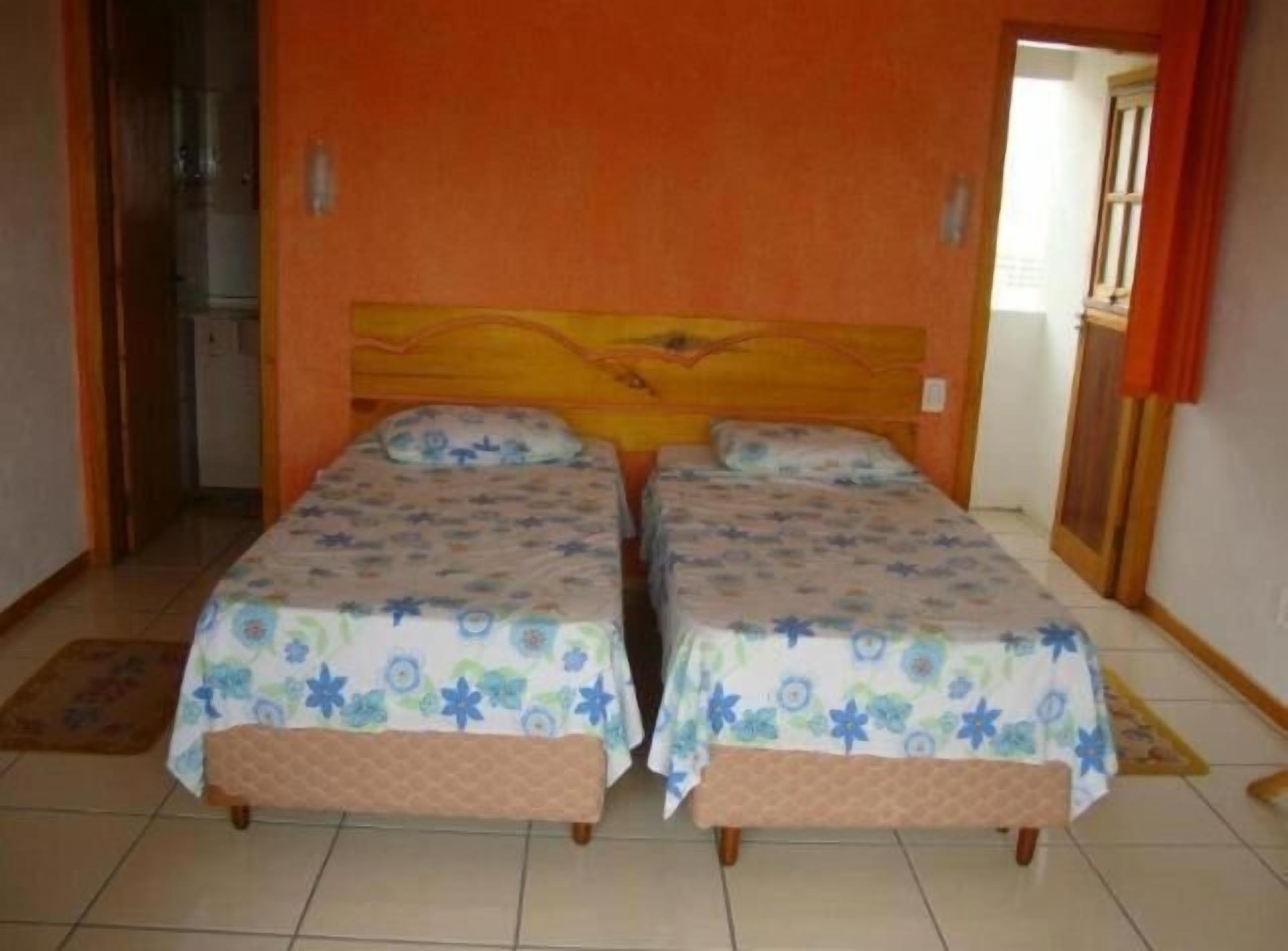 A room with two single beds, a wooden headboard, and a tiled floor.
