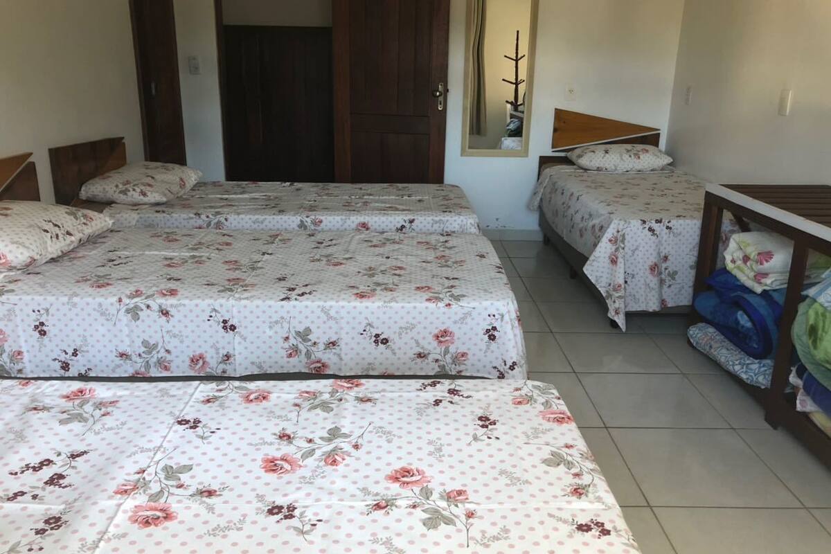 A dormitory room with two single beds, a wooden wardrobe, and a small table with folded blankets.