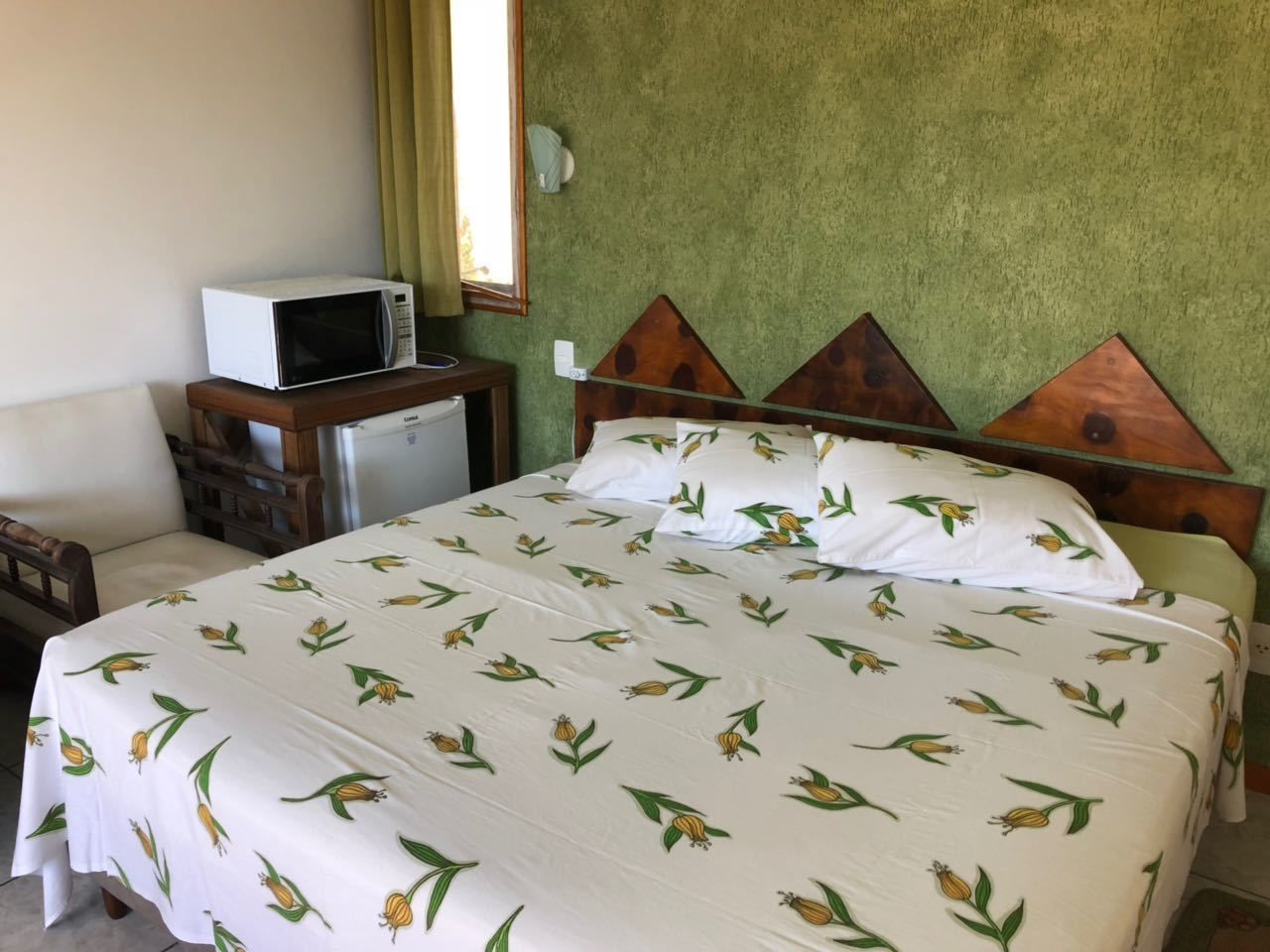 Una cama con colcha estampada, una mesita de noche con microondas y una pared verde con textura.