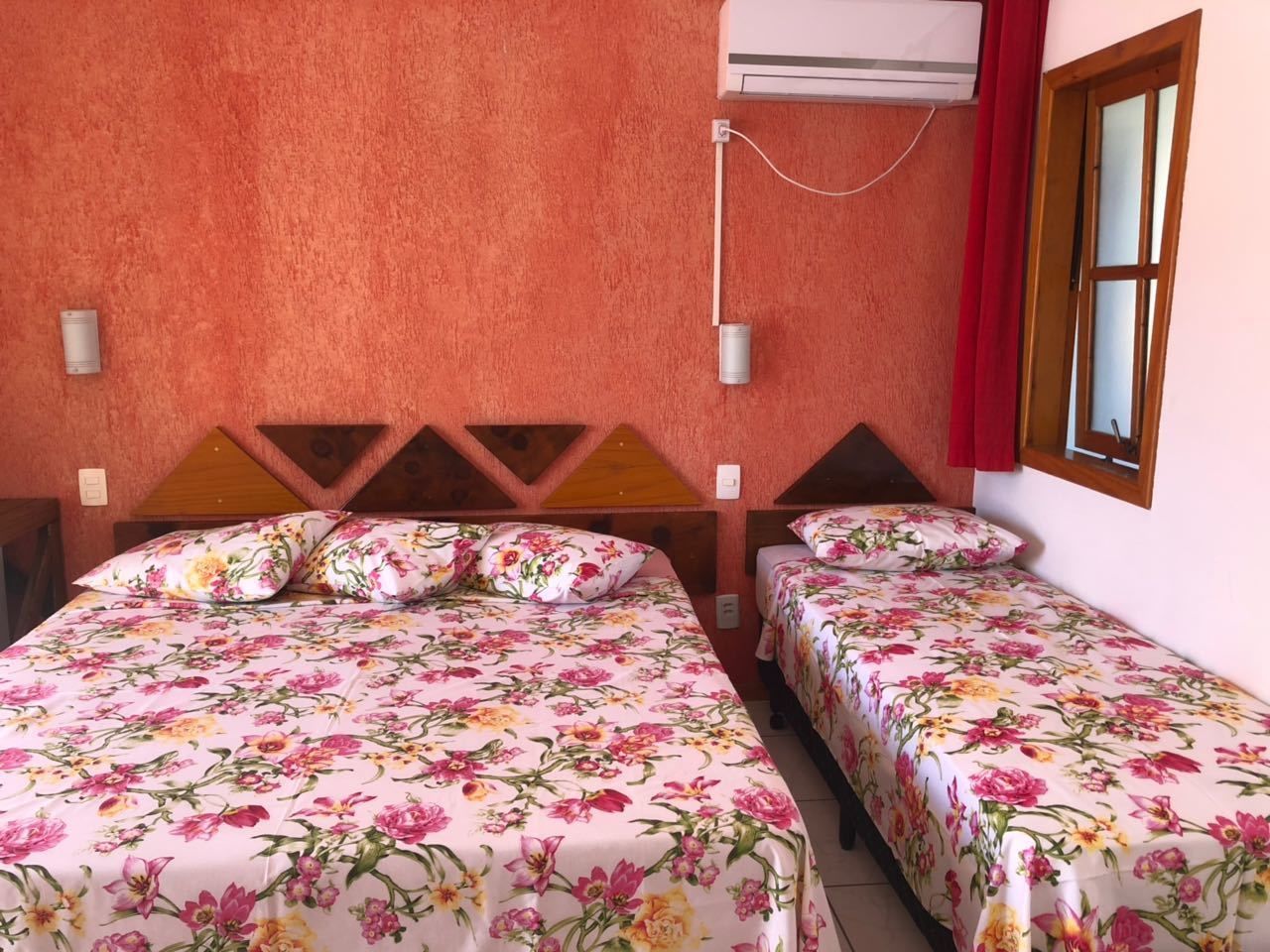 Una habitación con dos camas, cada una con ropa de cama floral, cabeceros de madera y cortinas rojas.