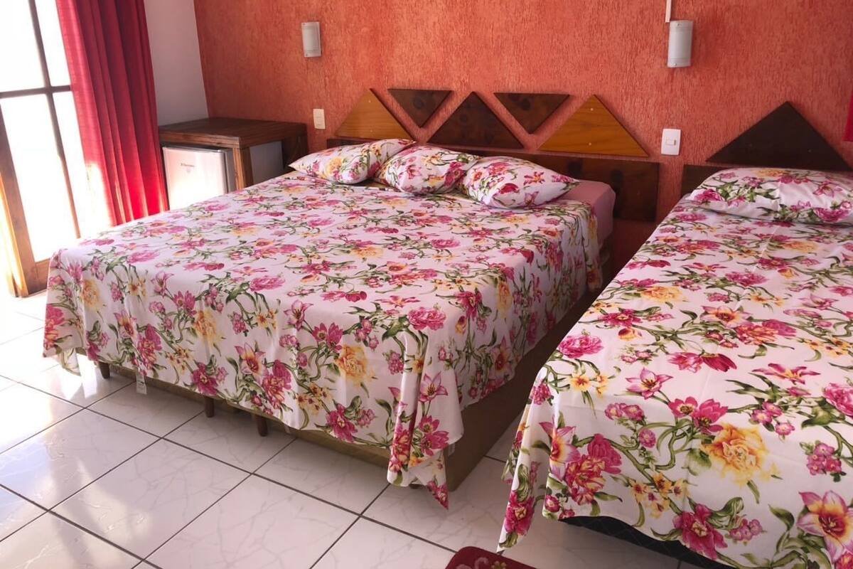 A hotel room with two beds, each with floral bedding, a red curtain, and a tiled floor.