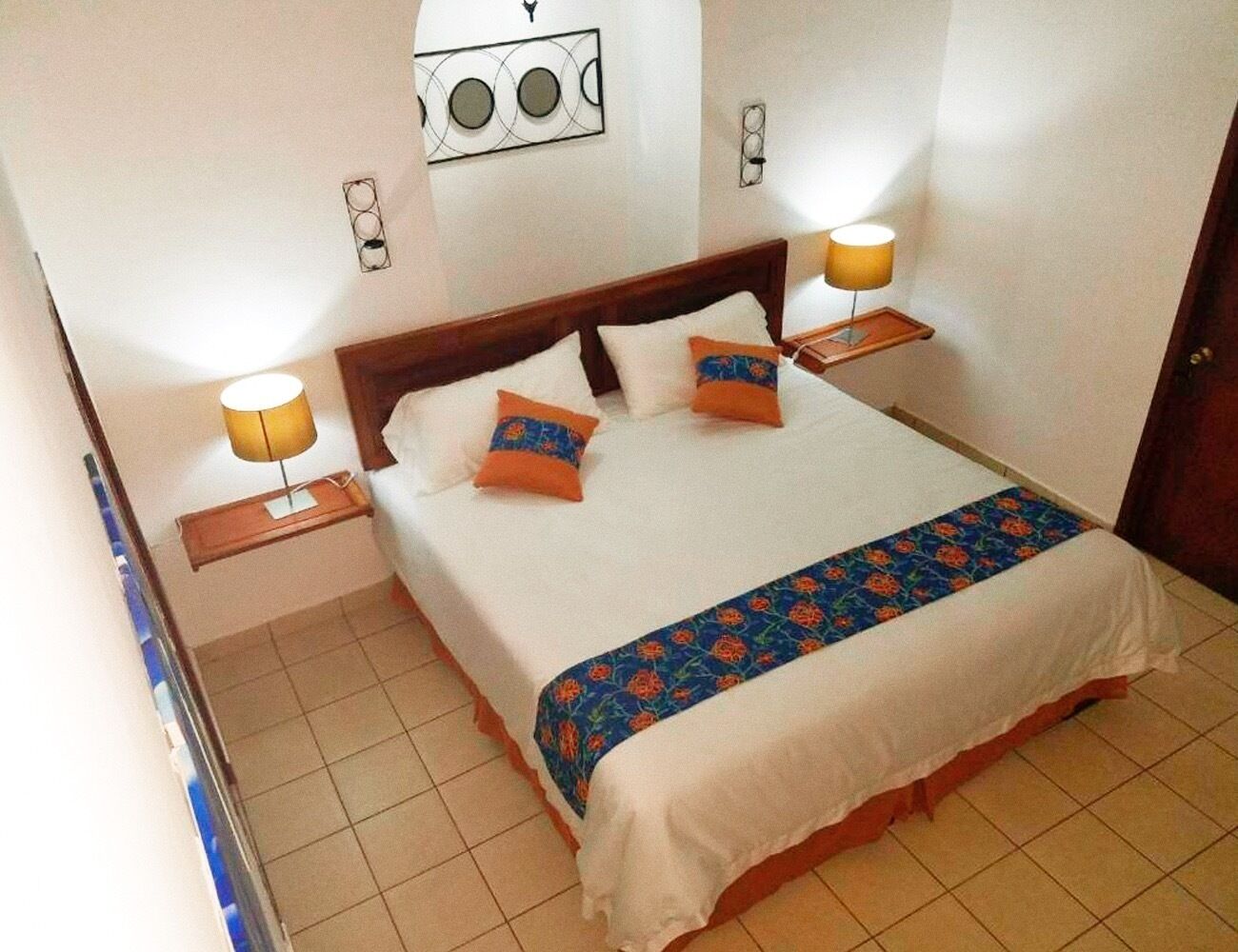 A neatly made bed with a patterned bedspread and pillows, two bedside lamps, and a wall clock.