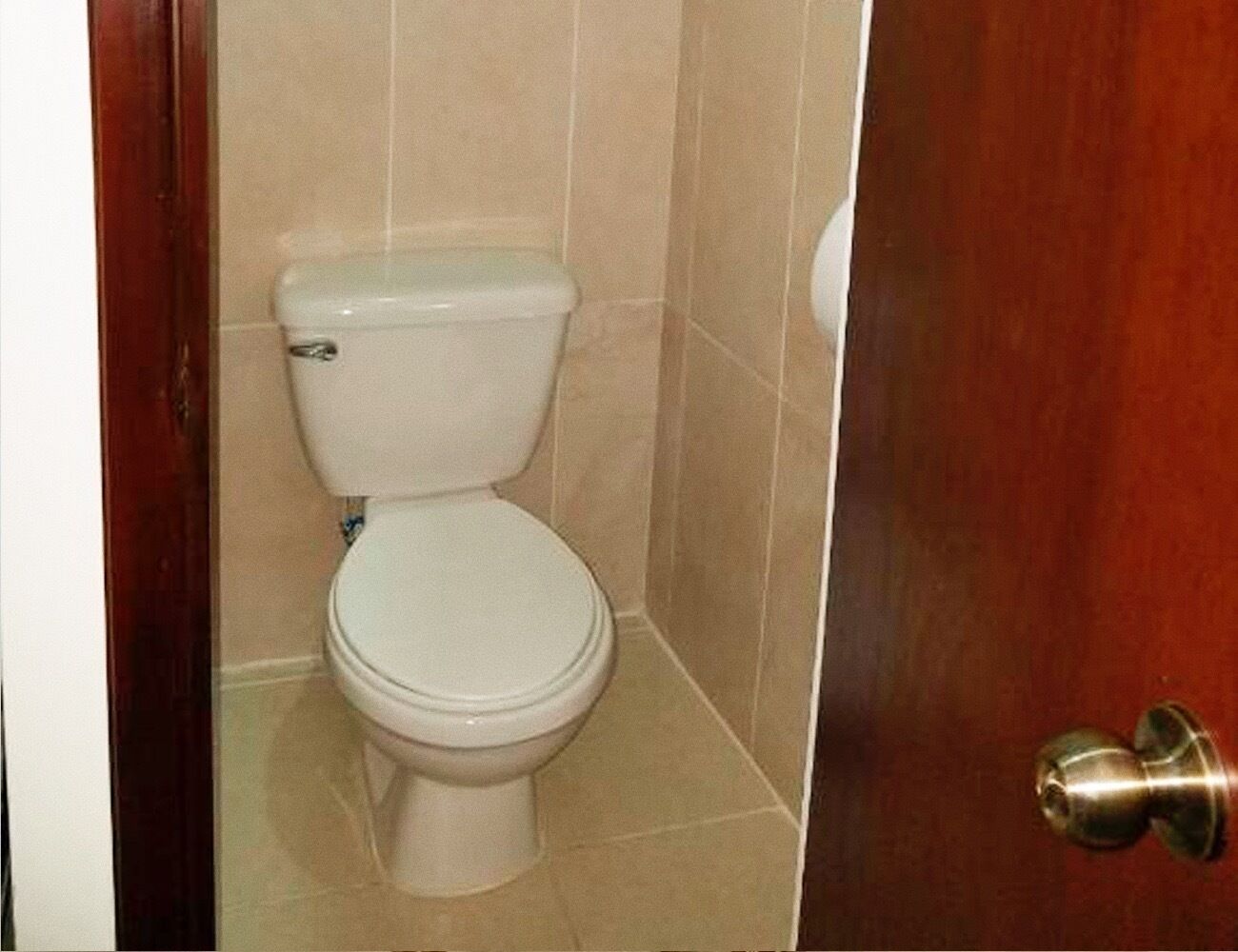 Un inodoro blanco estándar en un baño con azulejos color beige y una puerta de madera.