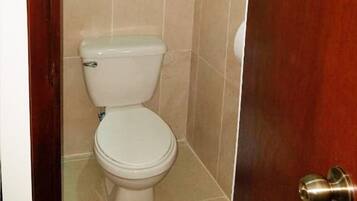Un inodoro blanco estándar en un baño con azulejos color beige y una puerta de madera.