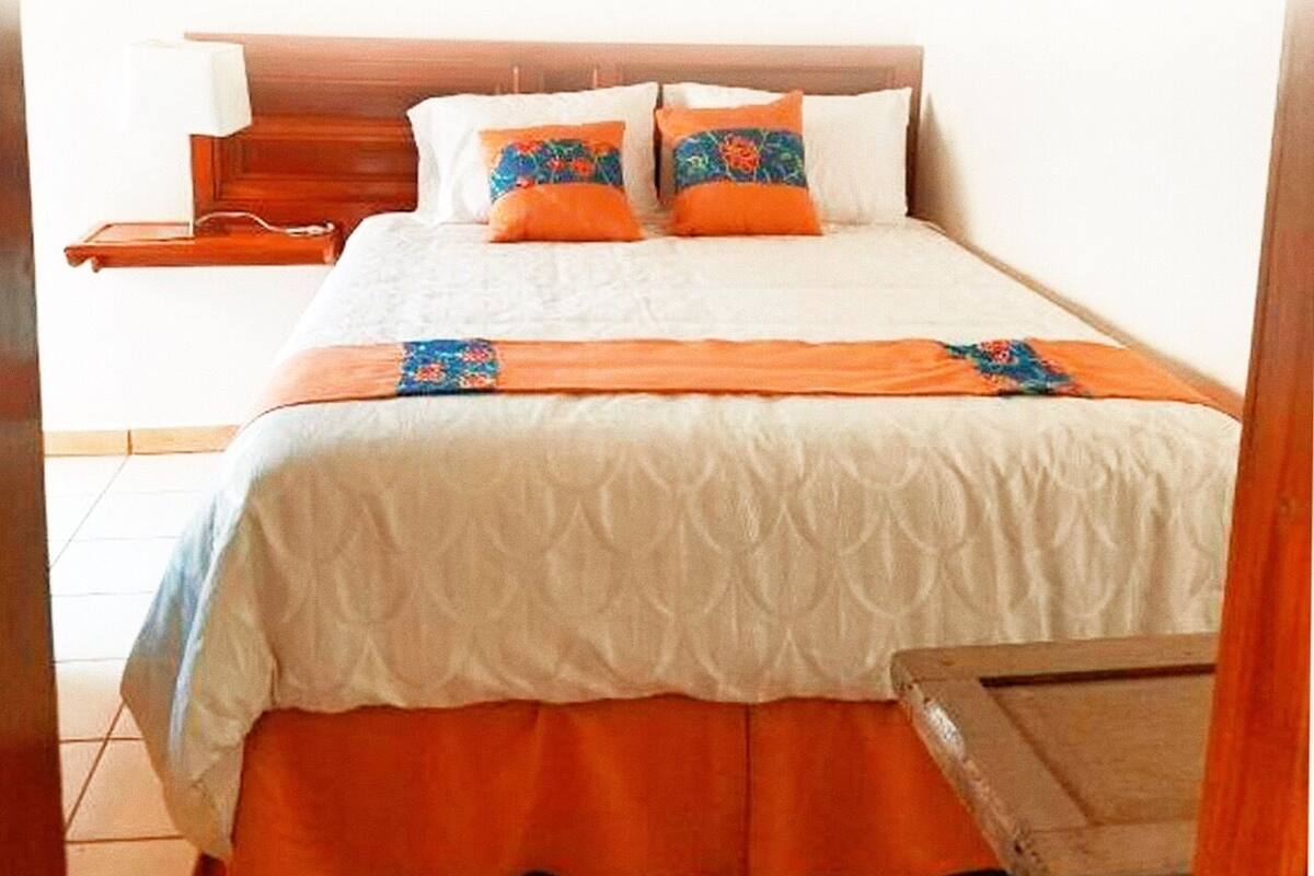 A bed with a white and orange bedspread, two orange pillows, and a wooden headboard.