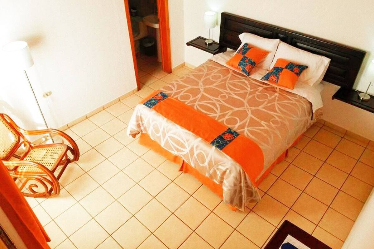 A hotel room with a bed, a nightstand, a chair, and a door leading to a bathroom.