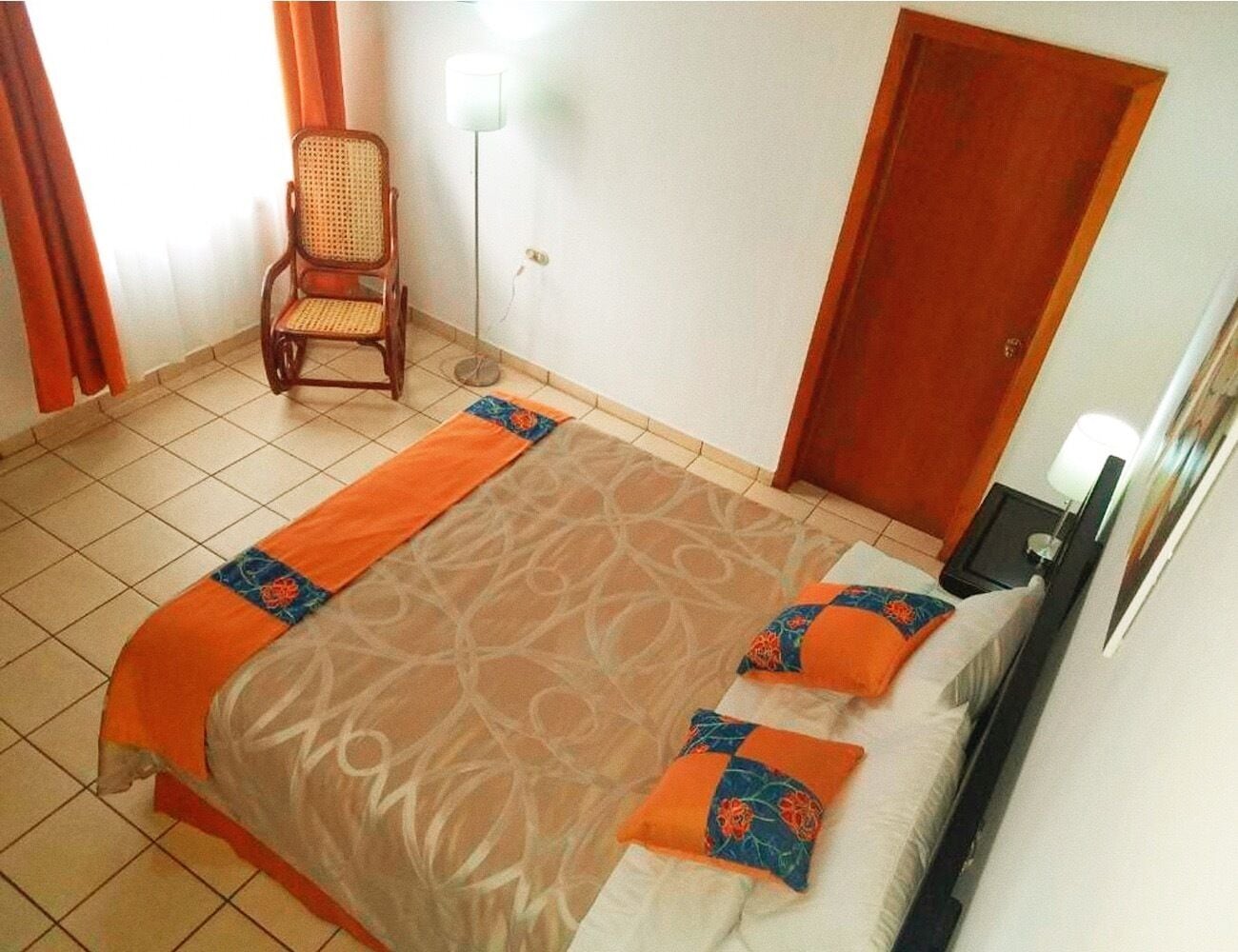 A hotel room with a bed, a chair, a nightstand, and a door.