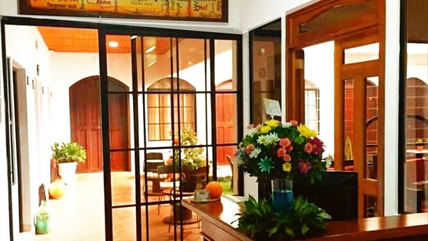 Un área de recepción con un mostrador de madera, un ventanal con vista al interior y un letrero sobre la puerta dando la bienvenida a los huéspedes.