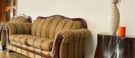 A vintage-style sofa with ornate wooden legs, a patterned rug, and a vase with dried plants on a wooden side table.