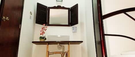 A small room with a wooden desk, a mirror, a sink, and a bed.