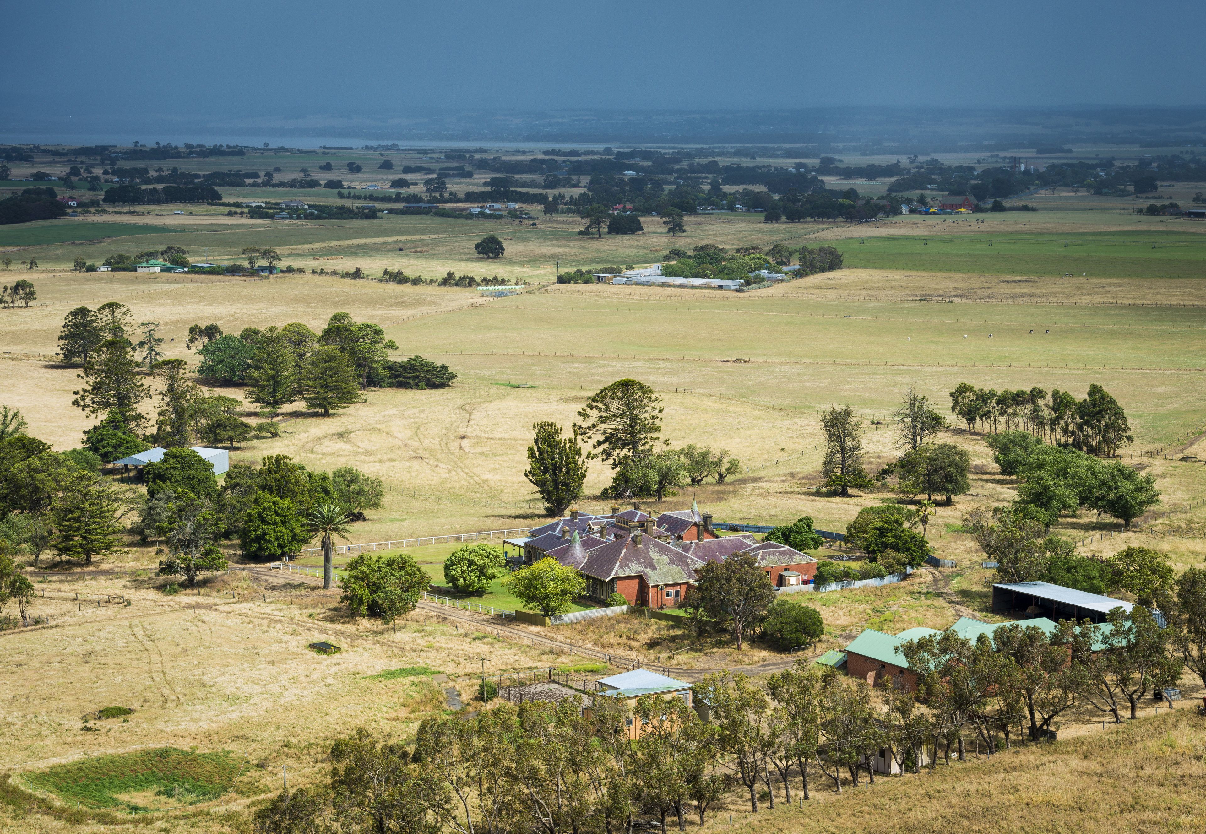 A rural landscape with a large house surrounded by fields and trees.