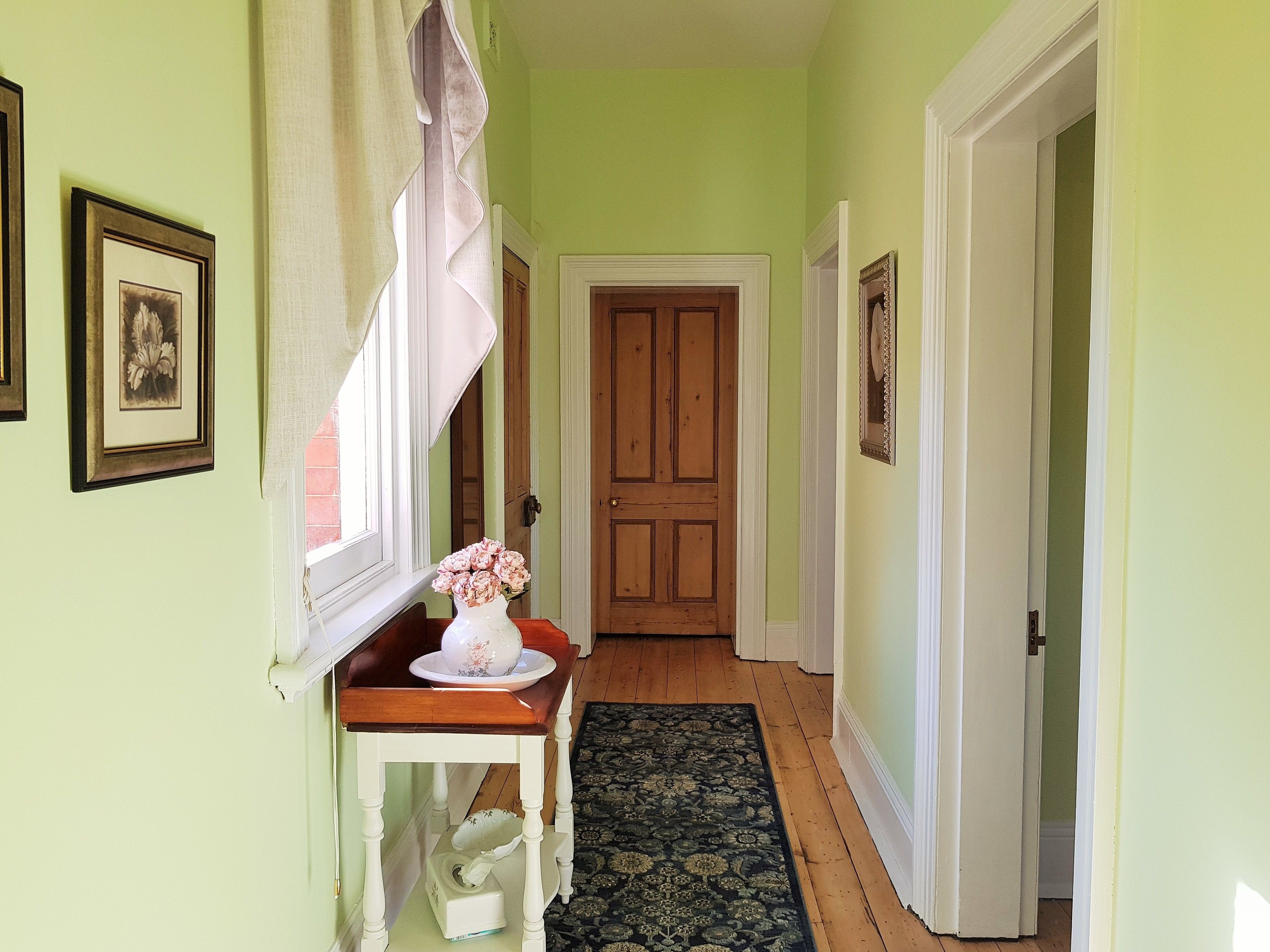 A hallway with a wooden door, a small table with a vase and a tissue box, and a patterned rug.