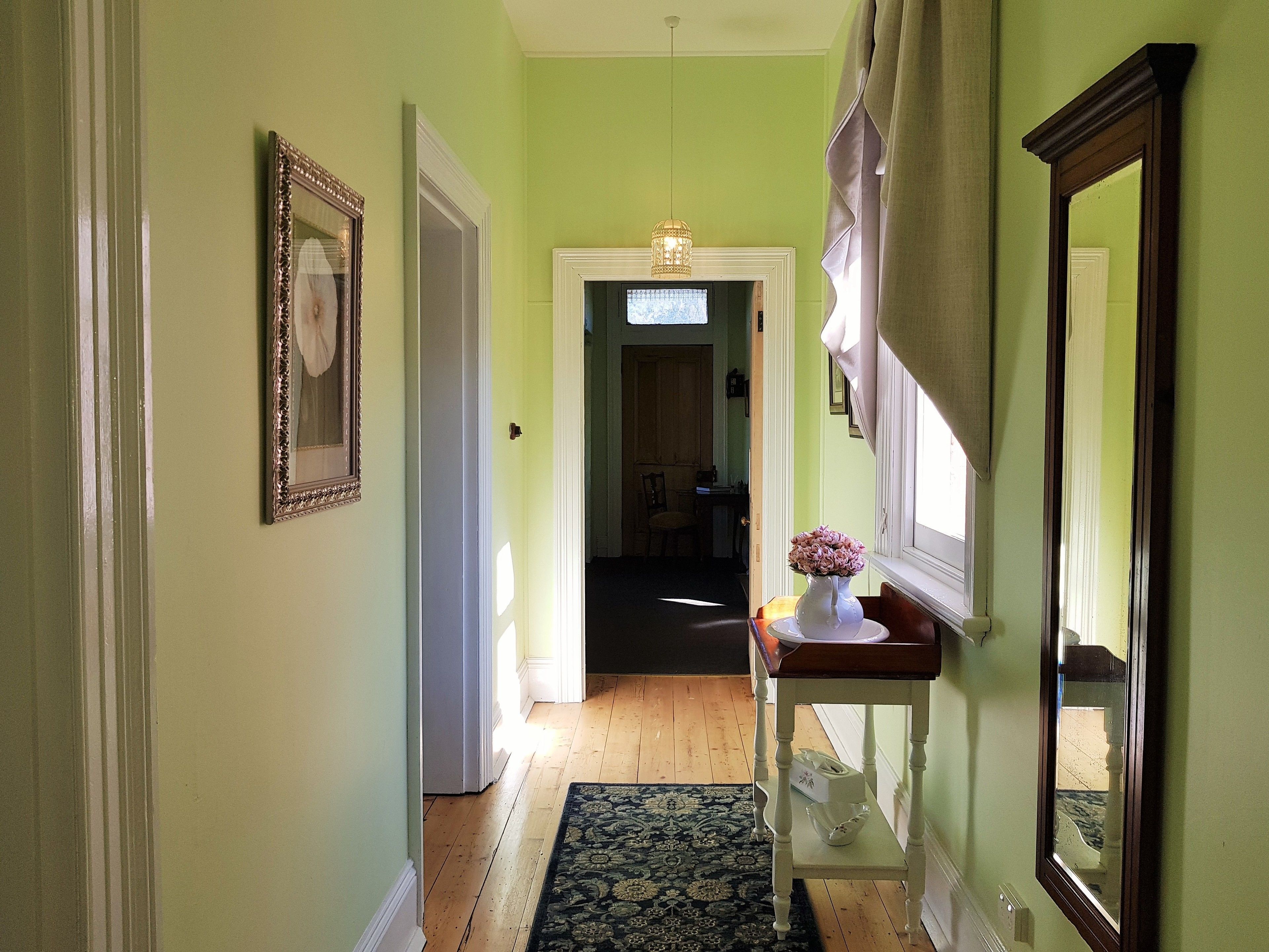 A hallway with a wooden floor, a rug, a vase with flowers on a table, and a mirror on the wall.