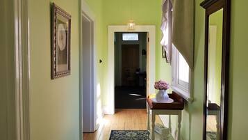 A hallway with a wooden floor, a rug, a vase with flowers on a table, and a mirror on the wall.